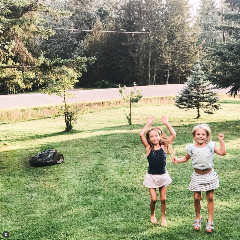kids playing in the grass with a Husqvarna robotic automower cutting the grass