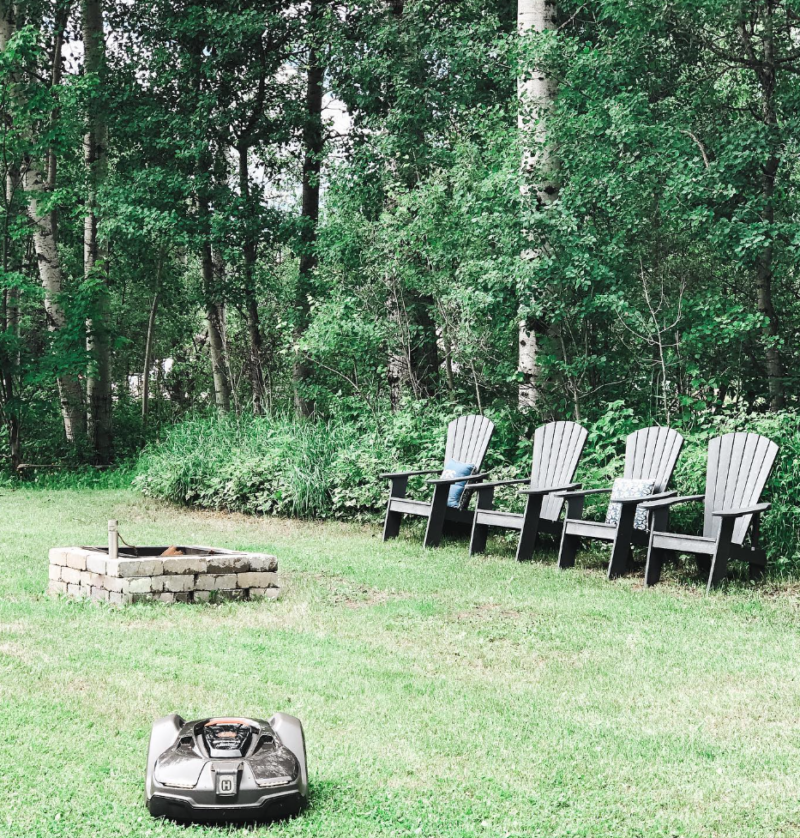 Husqvarna robotic automower cutting the grass in a large property with trees and a firepit